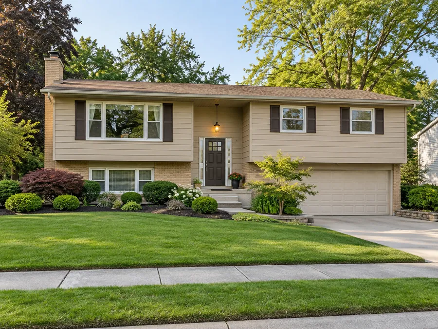 Illustrative AI concept: tan split-level house with fresh dark mulch, rounded shrubs and a crisp lawn edge tidy this split-level frontage. The limited palette improves definition while leaving the established trees and approach in place.