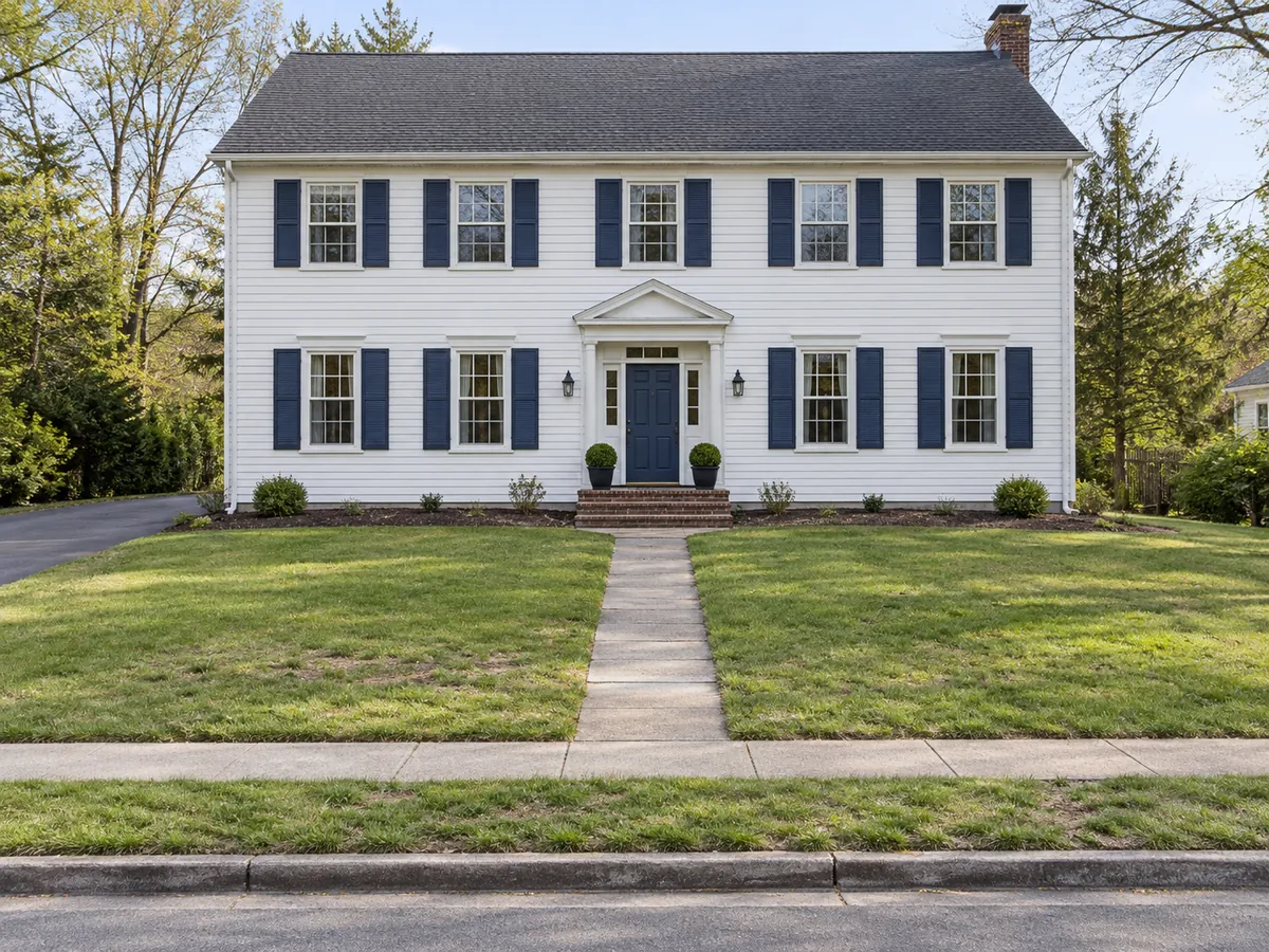 Illustrative AI concept: a bare colonial gains cottage flower beds while the lawn and walk stay. — Before
